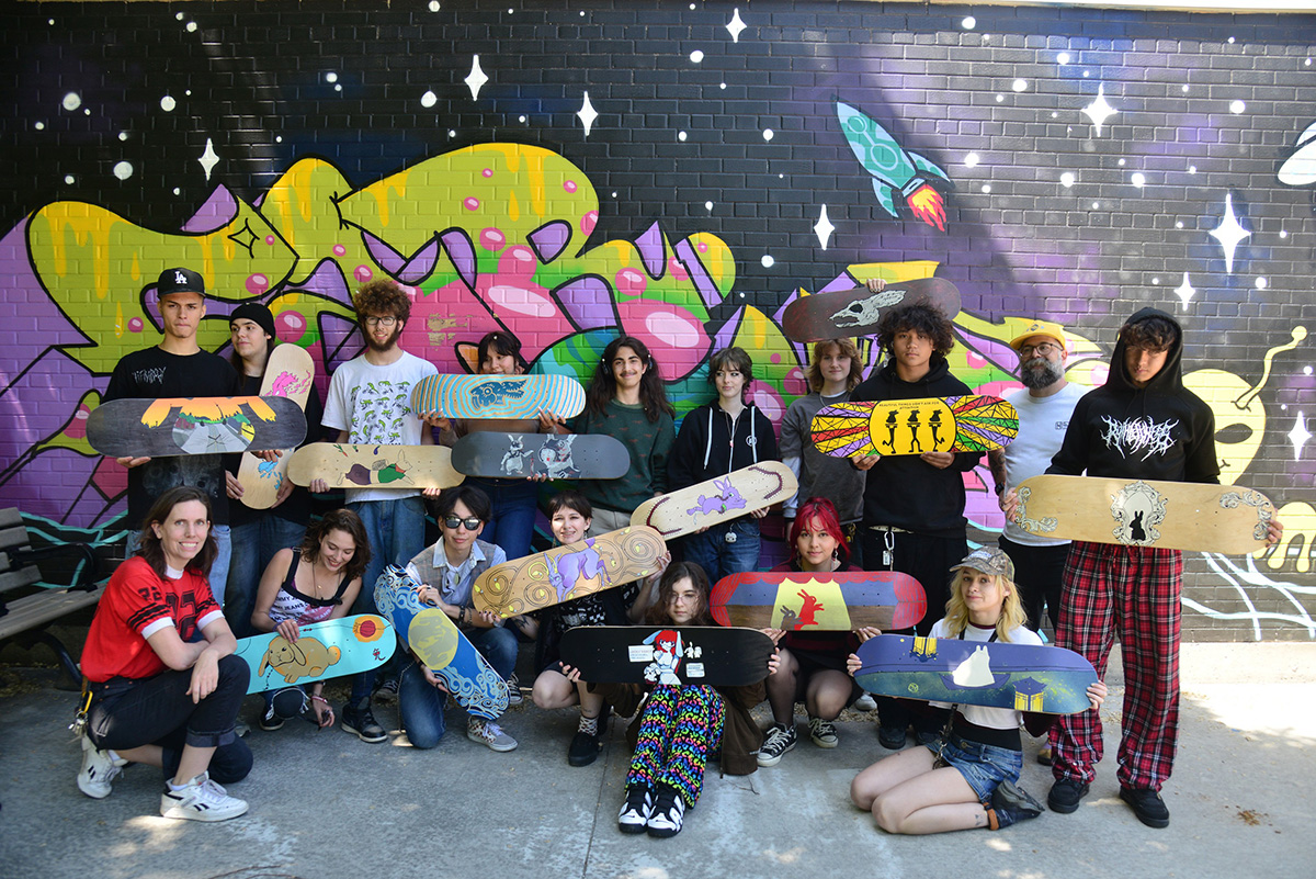 Group photo of students holding skateboards in front of mural