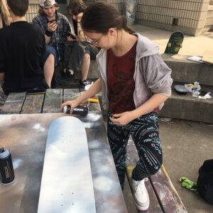 Student spray-paints a skateboard outside