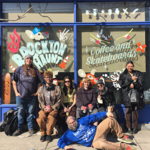 A group of students and their teacher pose outside the Brockton Haunt, coffee and skateboard shop